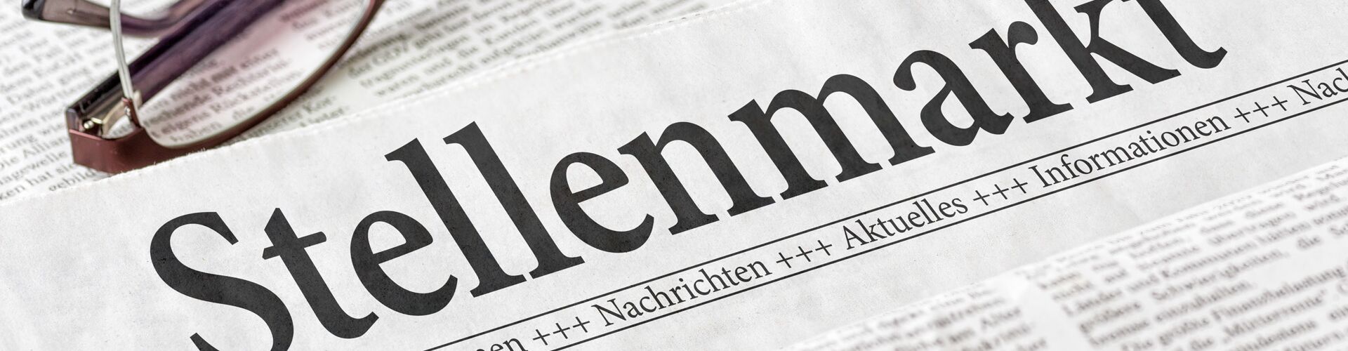 Zeitung mit der Headline Stellenmarkt, daneben liegt eine Lesebrille.