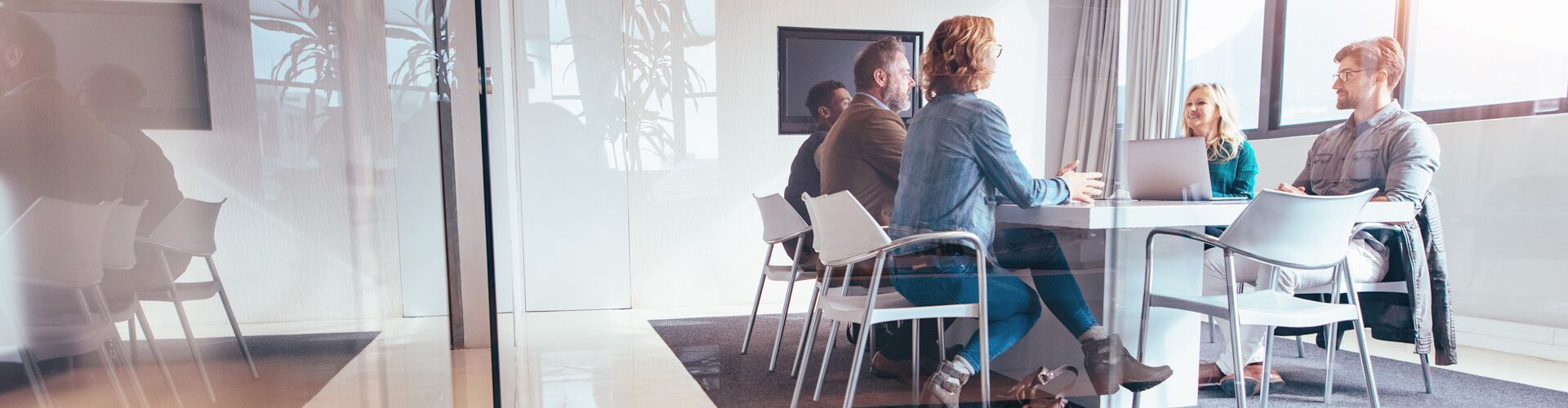 Fünf Personen sitzen in einem lichtdurchflutetem Besprechungszimmer